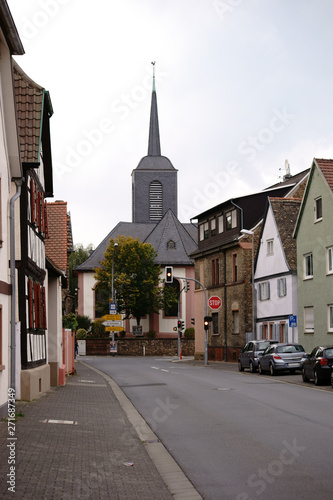 Der Turm der Marienkirche in Bischofsheim am Ende einer Hauptverkehrsstraße mit angrenzenden Wohnhäusern...