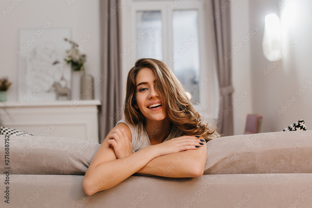 Naklejka premium Indoor portrait of lovely dark-haired woman lying on sofa with charming smile. Photo of carefree young lady posing with happy face expression, resting at home.