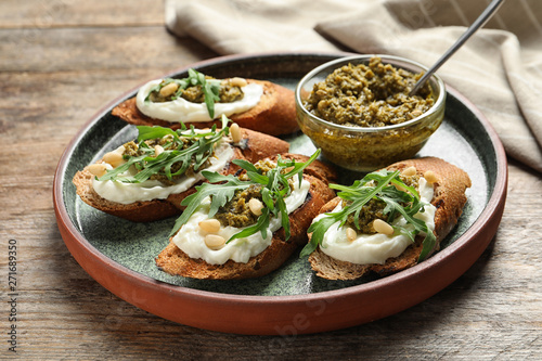 Plate with tasty bruschettas and pesto sauce on wooden table