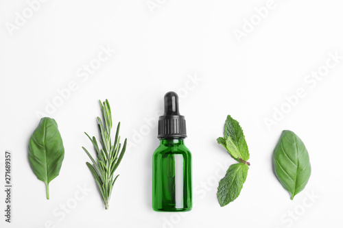 Little bottle of essential oil with different herbs on white background, top view