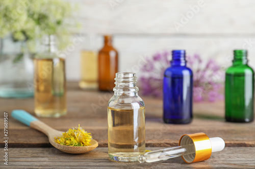 Bottle of essential oil, pipette and spoon with flowers on wooden table, space for text