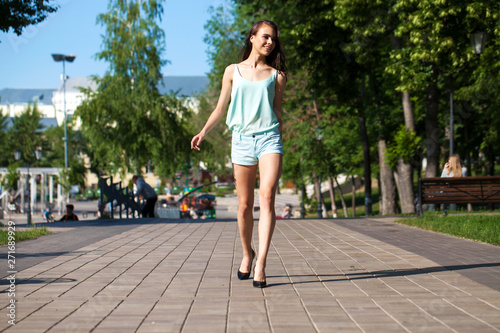 Young beautiful brunette woman in a blue blouse and shorts walking on the street