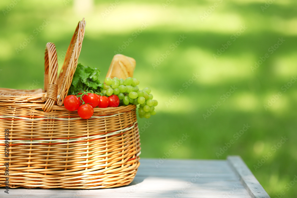 Wicker basket with food on table in park, space for text. Summer picnic Wicker basket with food on table in park, space for text. Summer picnic