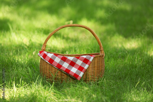 Wicker basket with blanket on green grass in park. Summer picnic