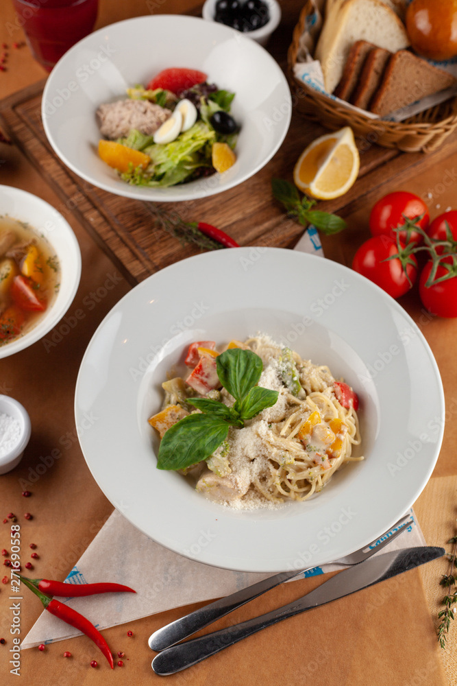 Close up of pasta with vegetables, chicken and creamy sauce, decorated with basil, served on a white table and as a part of set menu Close up of pasta with vegetables, chicken and creamy sauce, decorated with basil, served on a white table and as a part of set menu