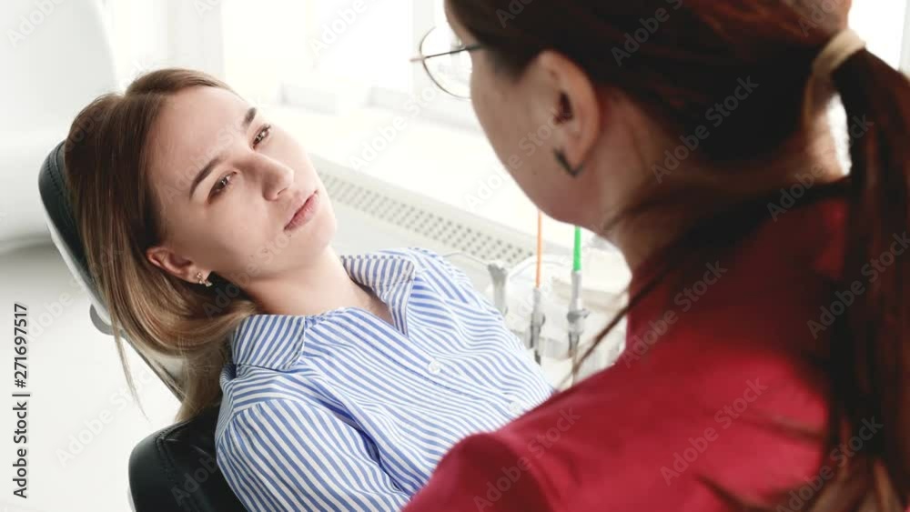 A young girl at a consultation with a dentist woman in glasses is sitting on a chair in a stamotology office. The conversation of the doctor and the patient A young girl at a consultation with a dentist woman in glasses is sitting on a chair in a stamotology office. The conversation of the doctor and the patient