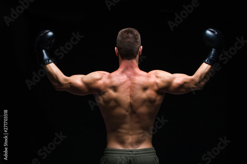 Powerful back. Muscular young man in black boxing gloves and shorts shows the different movements and strikes in the studio on a dark background. Strong Athletic Man - Fitness Model showing his