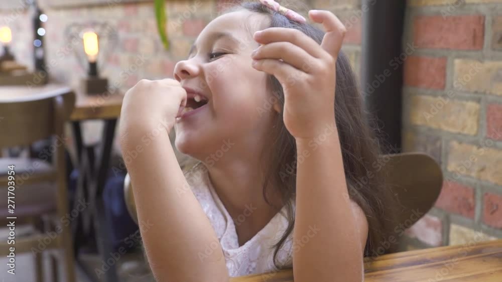 Portrait little girl eating sweet cake and smiling at table in cafe. Face cute girl smiling and eating sweet pie at dessert in restaurant. Portrait little girl eating sweet cake and smiling at table in cafe. Face cute girl smiling and eating sweet pie at dessert in restaurant.