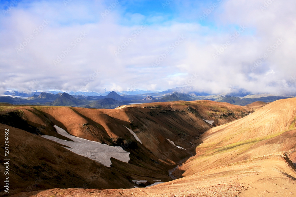 Orange sand hills with snow and green mountains in Landmannalaugar National Park, Iceland.