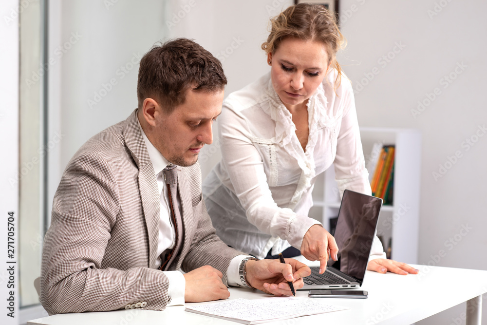 Half length portrait of  young  man wearing beige suit  sitting working on his laptop. A woman, a colleague, discusses the current business challenges.