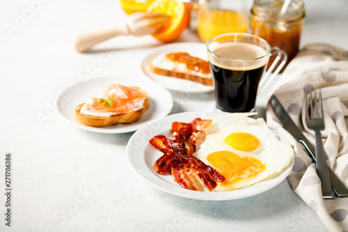 The English breakfast - eggs, bacon, toasts with ricotta and jam, juice in a glass, coffee on a grey background. Selective focus.