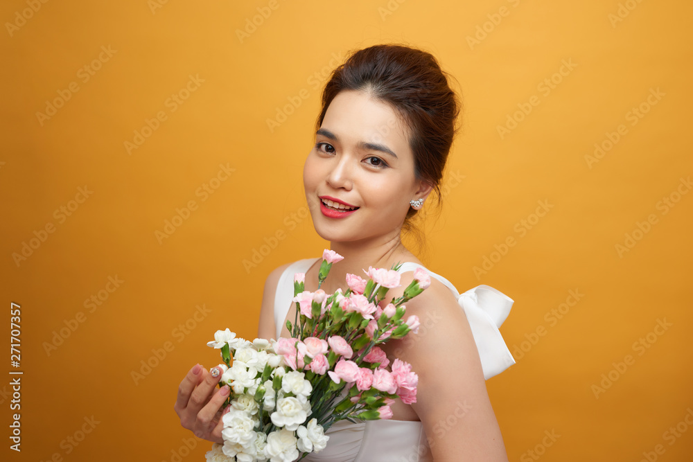 Portrait of a pretty young woman holding bouquet of carnation isolated over yellow background