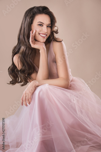 Attractive young brunette woman portrait in evening dress on the beige background