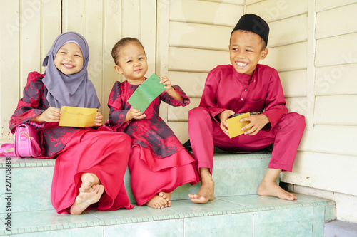 Three kids, happy siblings received money pocket or known as duit raya during Hari Raya Puasa or Eid Mubarak celebration. Muslim in Malaysian celebrate Eid with visiting other family and gathering