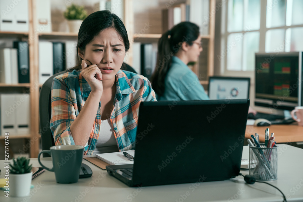 young concentrated asian woman employee indoors working with laptop computer thinking frowning confused. Coworking concept. female designer staring at notebook pc screen considering new project. young concentrated asian woman employee indoors working with laptop computer thinking frowning confused. Coworking concept. female designer staring at notebook pc screen considering new project.
