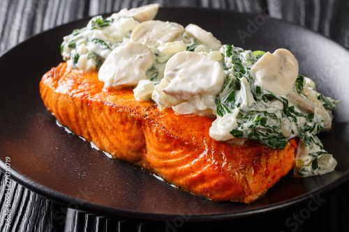 Florentine Salmon is simmered in a creamy wine sauce and topped with sauteed spinach and mushrooms close up on the plate. horizontal