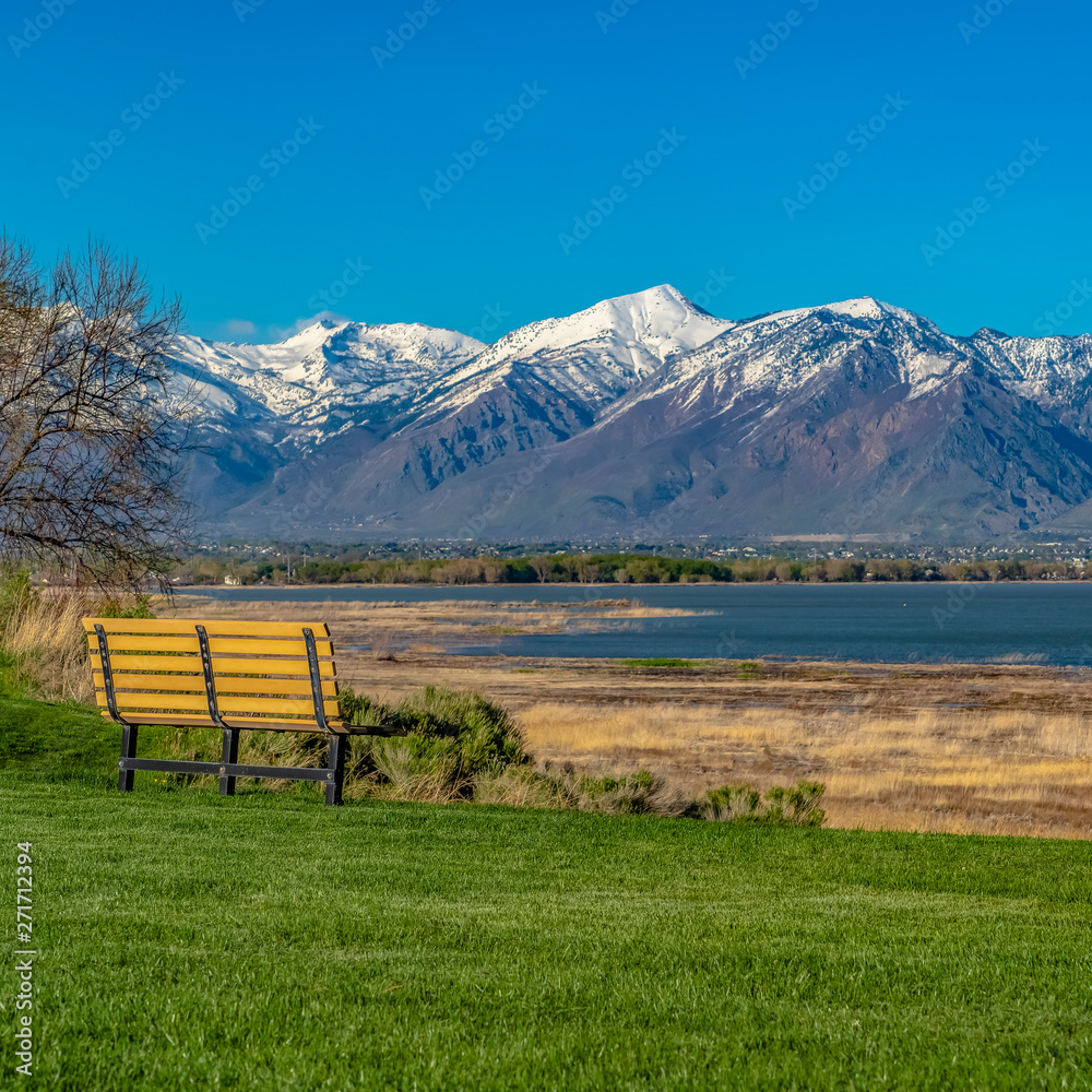 Square Bench on the lush field with a view of a lake and towering snow capped mountain