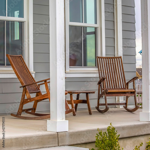 Frame Square Front porch of a house with brown rocking chairs and rectangular white pillars