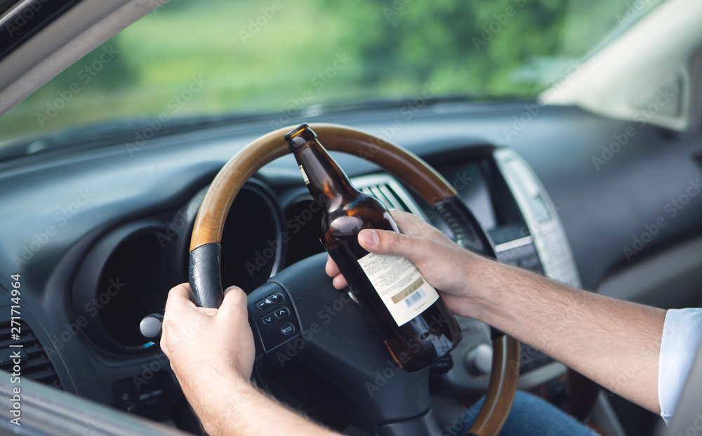 Drunk young man driving a car with a bottle of alcohol