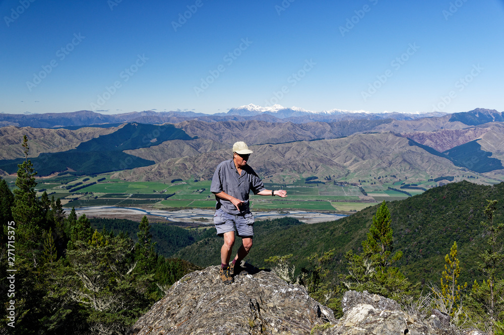 A man dances on a rocky outcrop, a valley and mountains form a backdrop