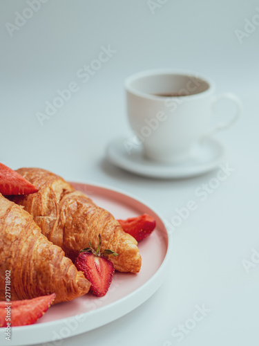 Summer morning with croissants, fresh breakfast with strawberry, and coffee. Closeup vertical shot with selective focus