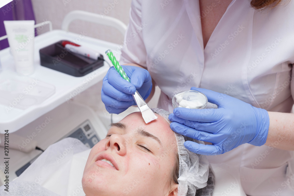 Crop master applying white mask with brush on face and neck of young woman in towel lying on table Crop master applying white mask with brush on face and neck of young woman in towel lying on table