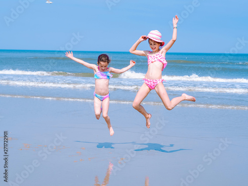 Two young happy girl having fun on tropical beach and jumping in swimsuit into the air on the sea coast at the day time. Summer travel and vacation concept