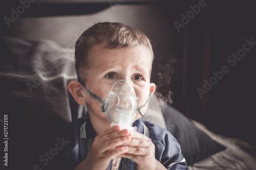 Two year old boy making inhalation with nebulizer at home.