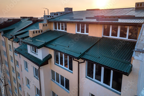 Aerial view of attic annex room exterior with plastic windows, roof and walls covered with green metal siding planks, new gutter system on top of high multi-storey apartment building.