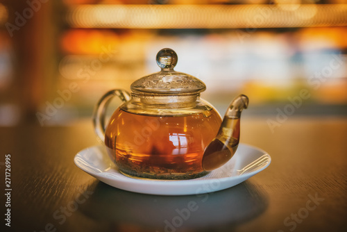 Glass teapot of invigorating fresh fragrant tea on a brown wooden table.