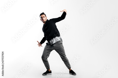 Stylish young dancer wearing a black sweatshirt and gray pants is dancing hip-poh on a white background