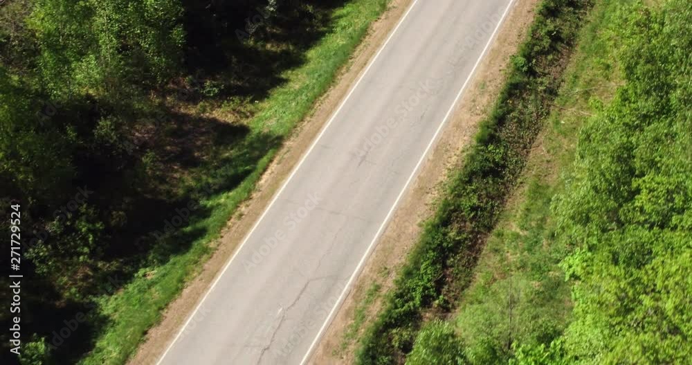 One dark car driving on empty wild asphalt road through green forest at summer sunny windy day - Aerial drone view One dark car driving on empty wild asphalt road through green forest at summer sunny windy day - Aerial drone view