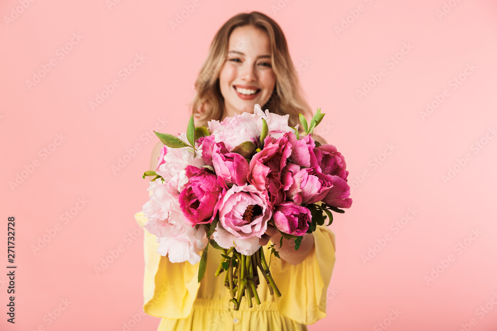 Young blonde woman posing isolated over pink wall background holding flowers