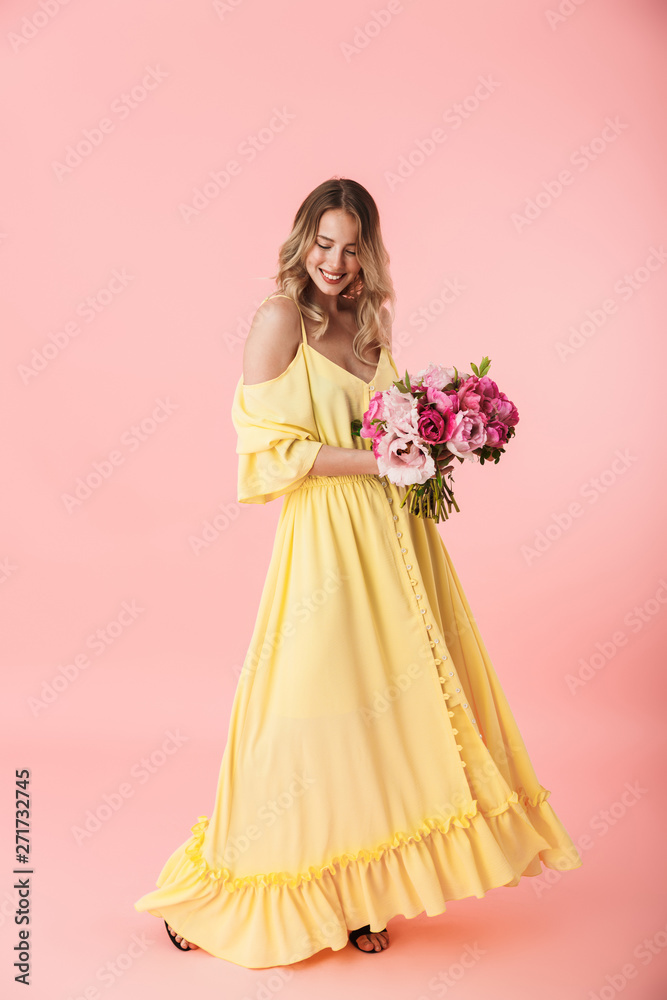 Young blonde woman posing isolated over pink wall background holding flowers