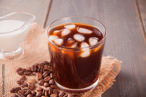 Iced latte coffee with ice cubes and coffee beans on a table.