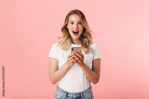Beautiful shocked young blonde woman posing isolated over pink wall background using mobile phone.