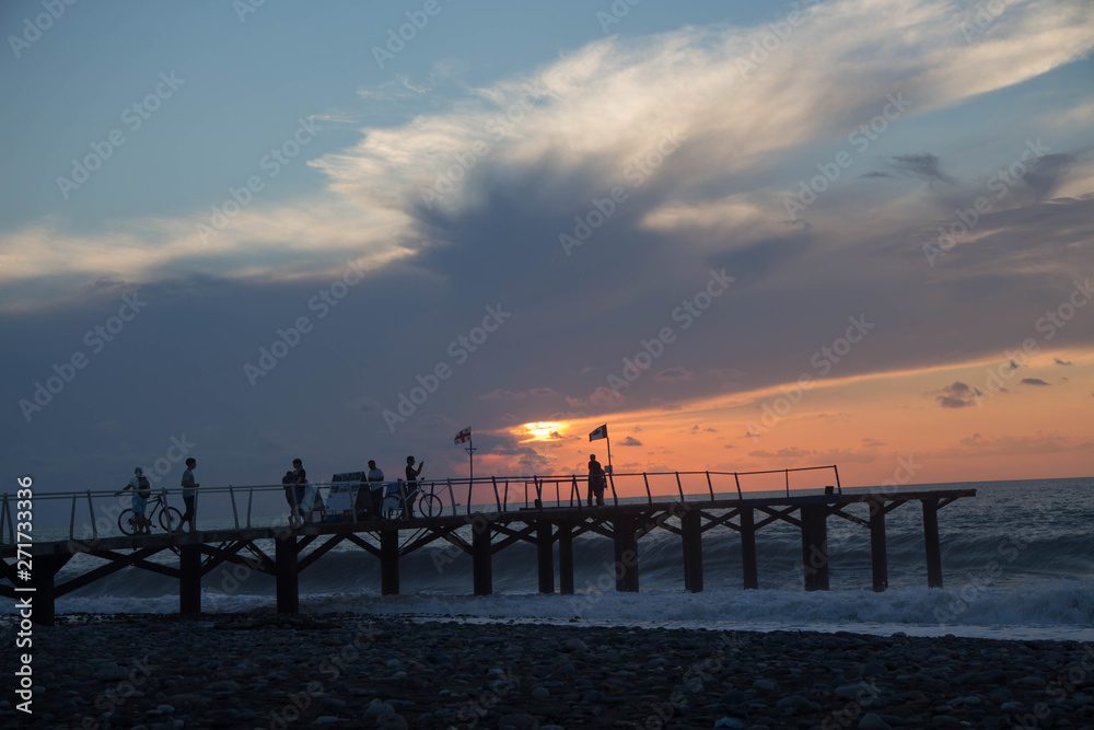 sun setting over Batumi beach Dock, as powerful waves roll in, and a very colorful sky is reflected on the beach