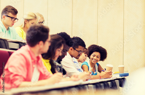 education, high school, university, learning and people concept - group of international students with notebooks and coffee writing test in lecture hall