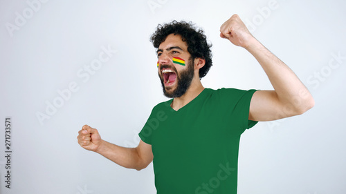 Sport fan screaming for the triumph of his team. Man with the flag of Bolivia makeup on his face and green t-shirt.