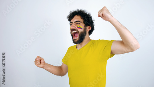 Sport fan screaming for the triumph of his team. Man with the flag of Ecuador makeup on his face and yellow t-shirt.