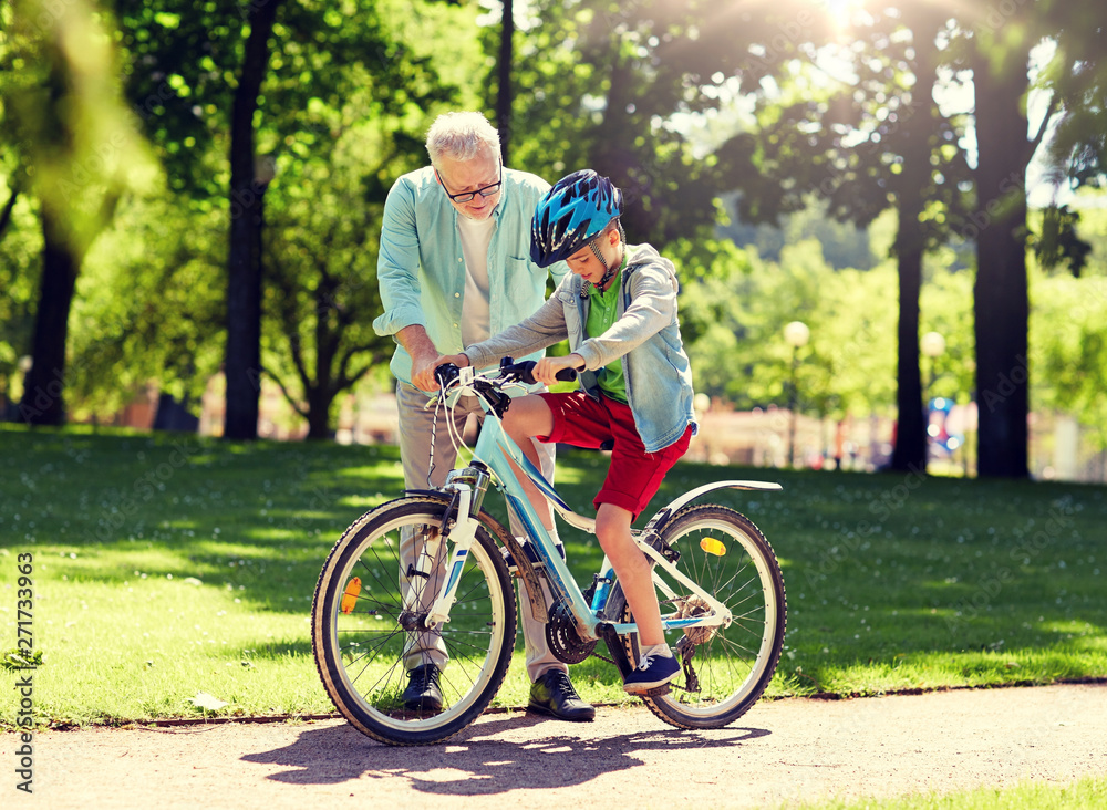 family, generation, safety and people concept - happy grandfather teaching boy how to ride bicycle at summer park