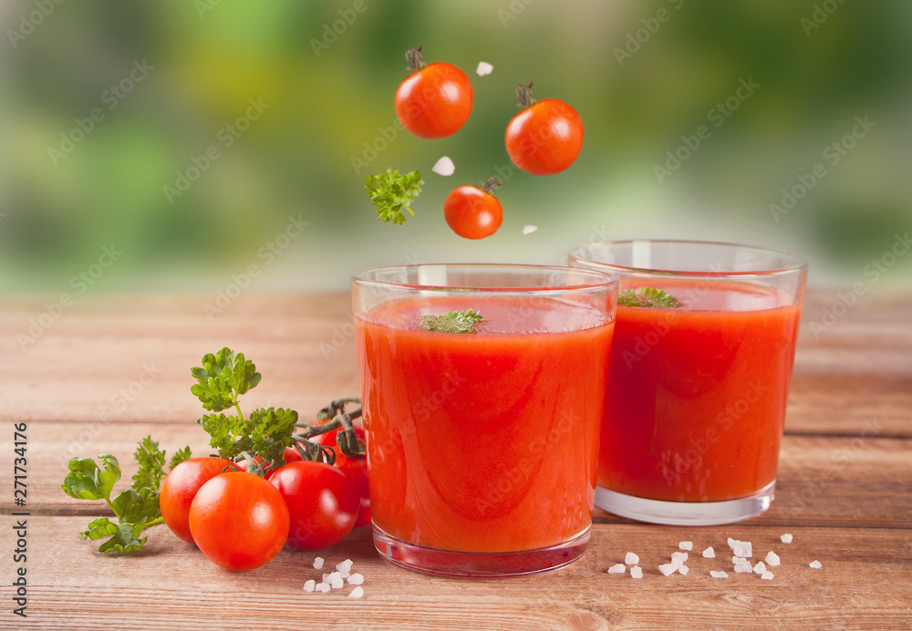 Tomato juice with parsley on the wooden table and flying cherry tomatoes Tomato juice with parsley on the wooden table and flying cherry tomatoes