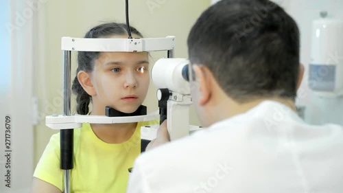 Male pediatric optometrist examining eyes of little girl with biomicroscopic slit lamp device photo