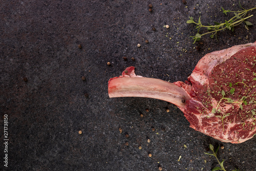 raw tomahawk steak on dark background with spices for grilling photo