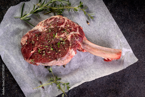 Foto raw tomahawk steak on dark background with spices for grilling