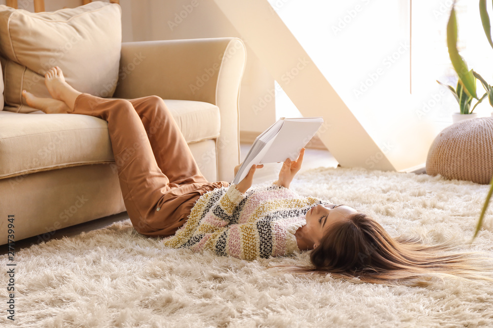 Beautiful young woman reading book while lying on floor at home - obrazy, fototapety, plakaty 