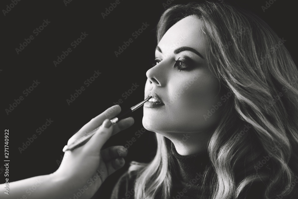 Obraz premium Beauty shop. Make up. Hand of stylist paints lips with a brush to client. Black and white photo.