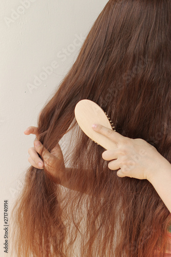 girl with long brown hair combing them with a wooden comb, holding strands, vertical, close-up