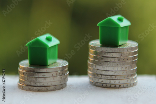 models of houses are located on stacked stacks of coins on a growing on the table on a blurred green natural background, the concept of money growth photo