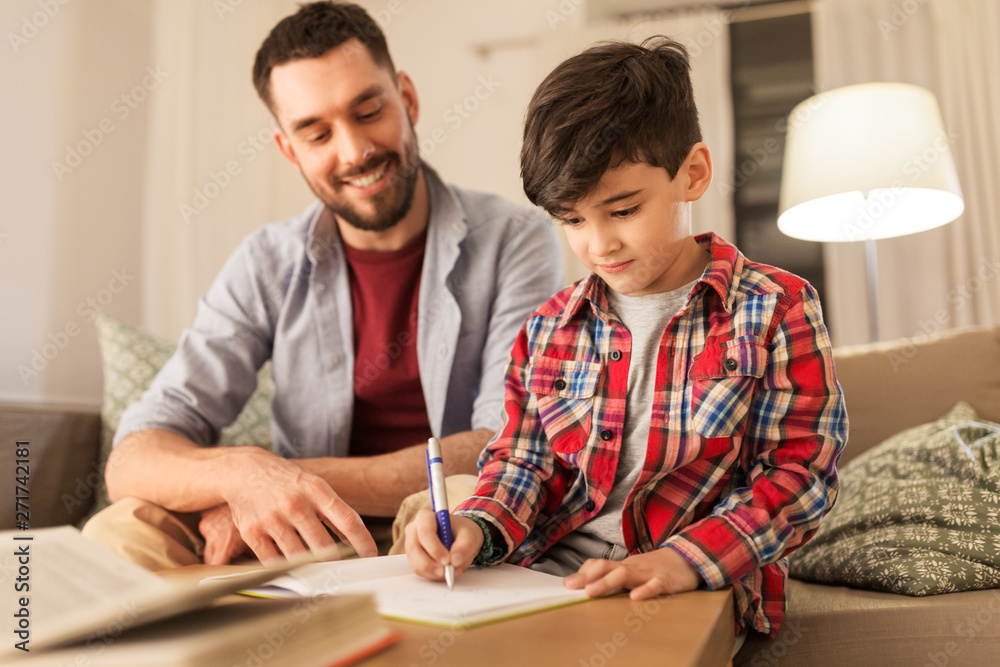education, family and homework concept - happy father and son with book writing to notebook at home education, family and homework concept - happy father and son with book writing to notebook at home